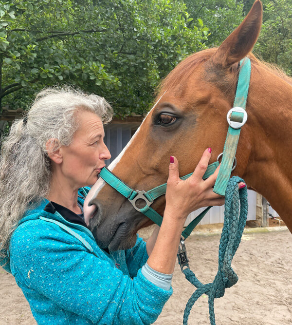 Annely und ihr Pferd, eine Seitenansicht, wie sich Pferd und Besitzerin anschauen, dabei hat sie mit ihren Händen den Pferdekopf geschlungen.